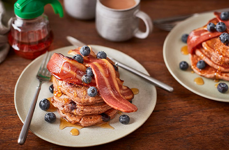Enjoy a stack of fluffy vegan blueberry pancakes for brunch, topped with maple syrup and crispy rashers of meat-free smoky bacon for a weekend treat!