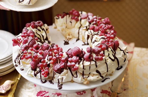 This Christmas pud is an absolute showstopper: a pavlova meringue wreath adorned with whipped cream, juicy berries and decorated with an unctuous chocolate sauce made with cream, golden syrup, butter and melted dark chocolate.