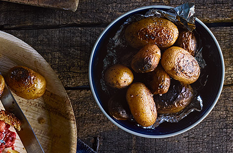 These charred potatoes make a delicious side dish and can be cooked on a barbecue, in the embers of a bonfire, or in the oven. With a hint of spice from cayenne pepper, the tender potatoes are served with a delicous creamy herb dip.